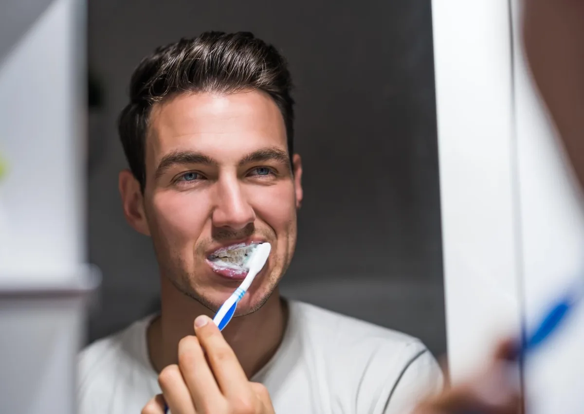 Man gently brushing his teeth as part of his daily oral hygiene routine to support dental implant recovery and long-term maintenance.