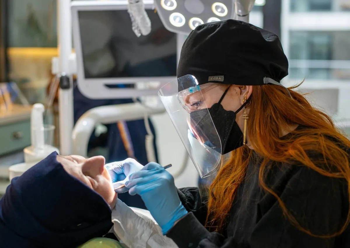Dental professional examining a patient's teeth during a consultation to evaluate tooth replacement options and explain the differences between dentures and dental implants.