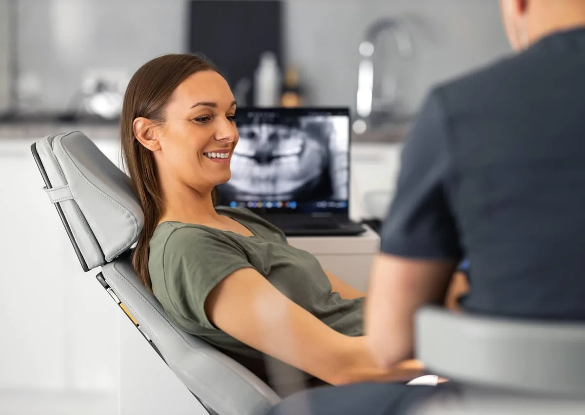 Patient discussing single tooth implant cost and treatment options and recovery with a dentist during a consultation, with a dental X-ray in the background.